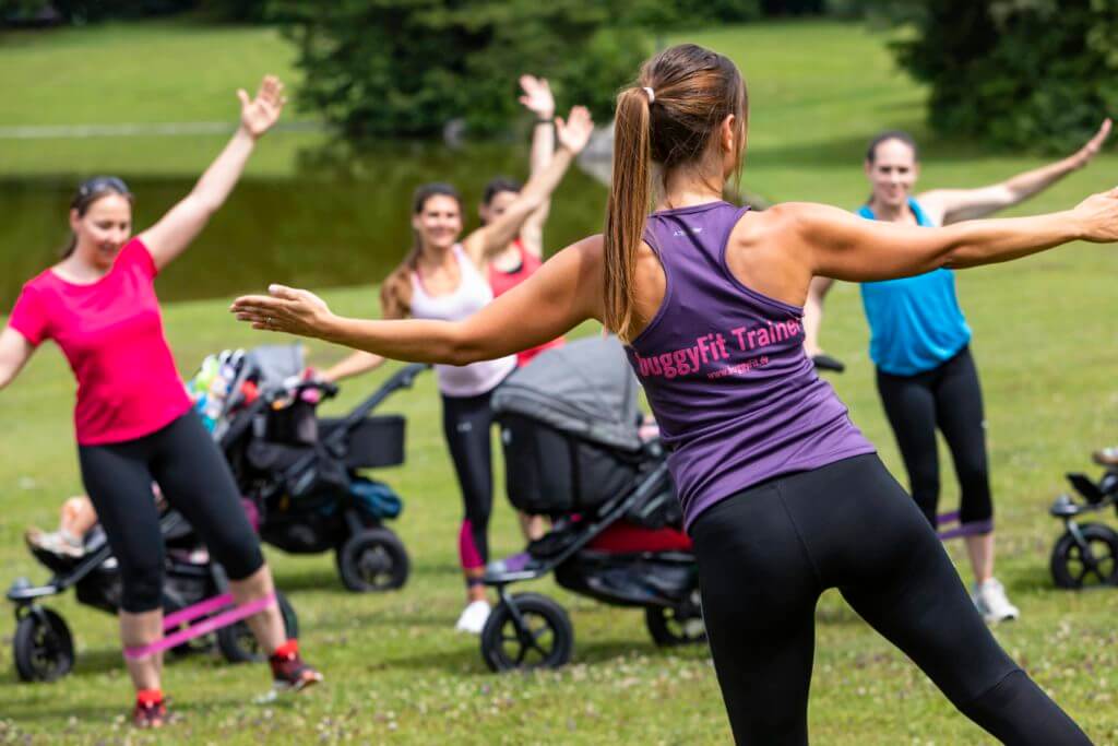buggyFit Trainerin leitet einen Kurs mit Mamas und Kinderwagen im Park