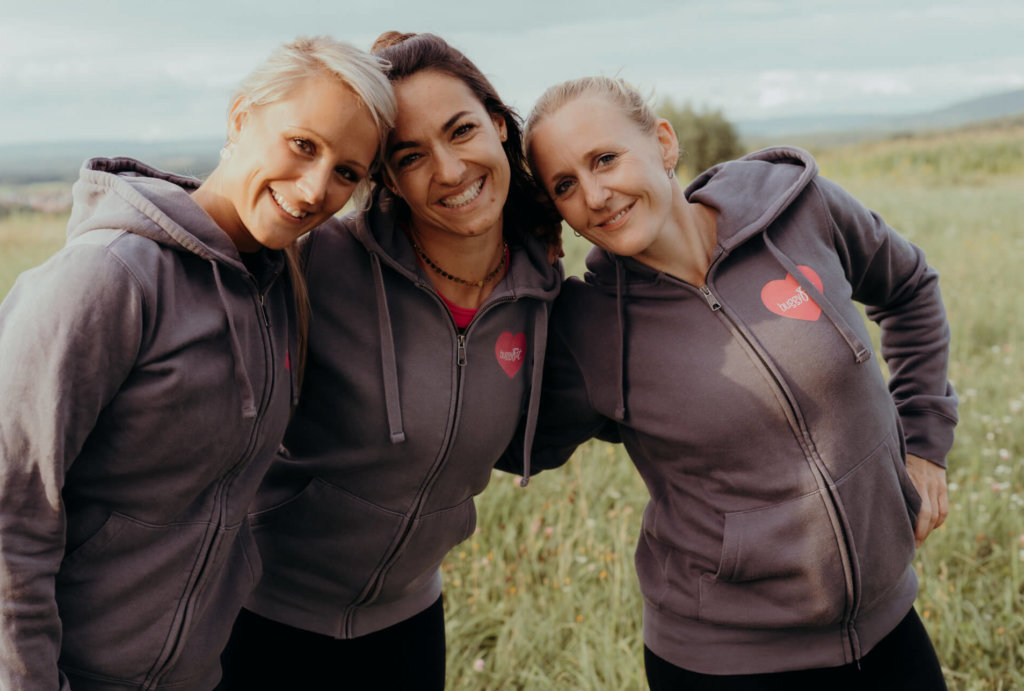 Drei Fitnesstrainerin, im gleichen Outfit auf der Wiese mit grauen Hoody,