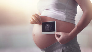 Pregnant woman holding ultrasound scan on a light background