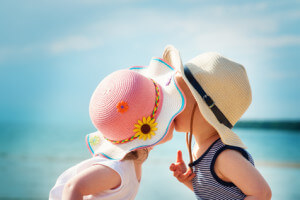 Babygirl and babyboy kissing on the beach in straw hats