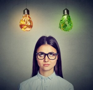 Woman in glasses thinking looking at junk food and green vegetables light bulb isolated on gray background.