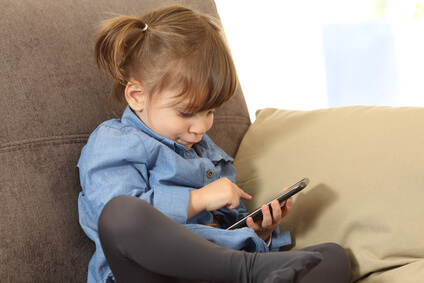 Concentrated baby playing games with a smart phone on line sitting on a sofa in the living room at home