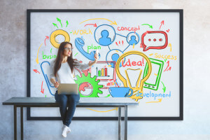 Womanwith laptop sitting on table and taking selfie with smartphone. Frame with business sketch in the background. Technology concept