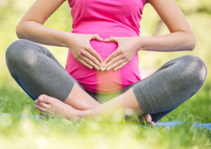 Beautiful pregnant woman sitting on rubber mat in summer park.