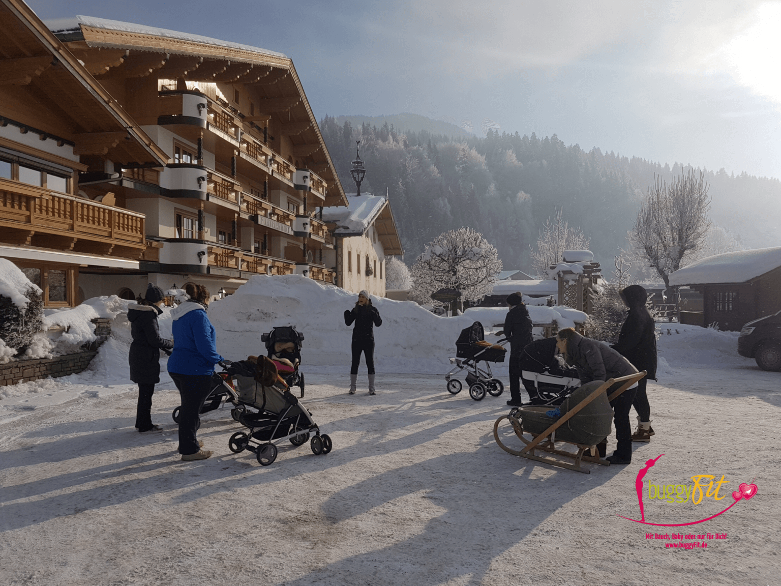 buggyFit-Kurs im Schnee: Trainerin leitet eine Gruppe Mamas mit Kinderwagen im Winter an