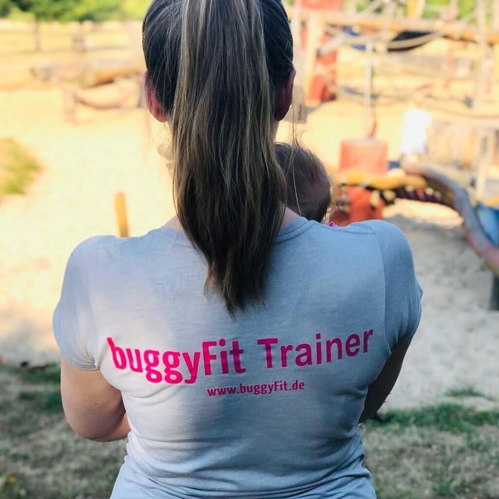 buggyFit Trainerin mit Baby auf dem Arm von hinten fotografiert.