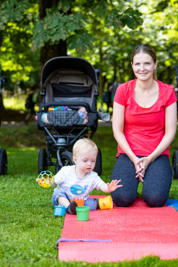 Mama sitzt nach dem Sport auf der Fitnessmatte und das Baby spielt.