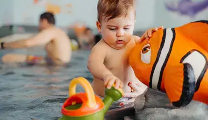 Baby spielt im Wasser in einem Babybecken mit Gießkanne und Fisch.