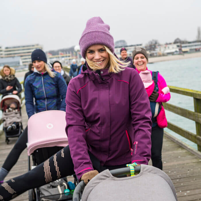 Glücklich Mamagruppe macht Sport. Eine Mama hebt das Bein. Mamas mit Kinderwagen und Babytrage.