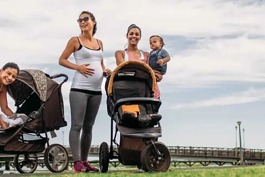 Eine Schwangere und eine Mama mit Baby auf dem Arm lachen gemeinsam, daneben stehen Kinderwagen
