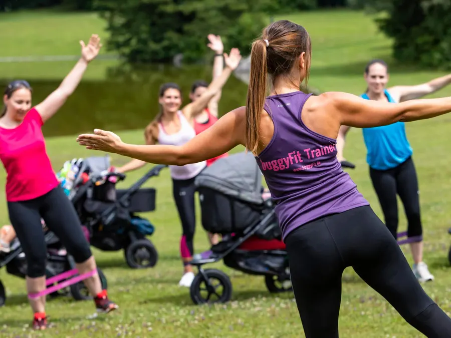 Vier buggyFit-Trainerinnen klatschen sich im Park ab, Kinderwagen stehen daneben