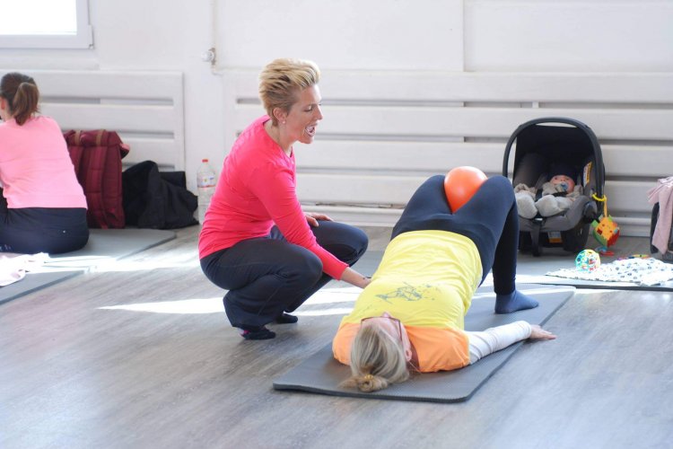 buggyFit Trainerin begleitet eine Mama bei einer sanften Rückbildungsübung, Baby daneben