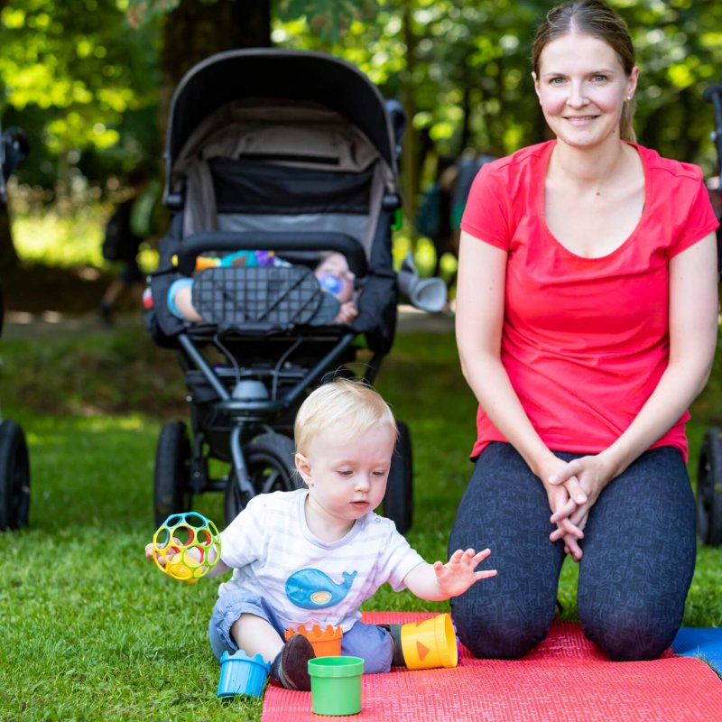 Mama sitzt nach dem Sport auf der Fitnessmatte und das Baby spielt.