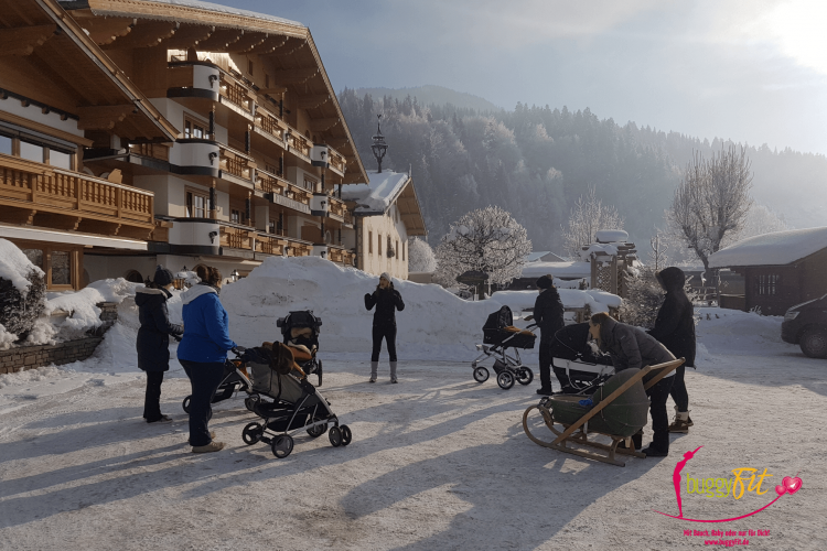 buggyFit-Kurs im Schnee: Trainerin leitet eine Gruppe Mamas mit Kinderwagen im Winter an